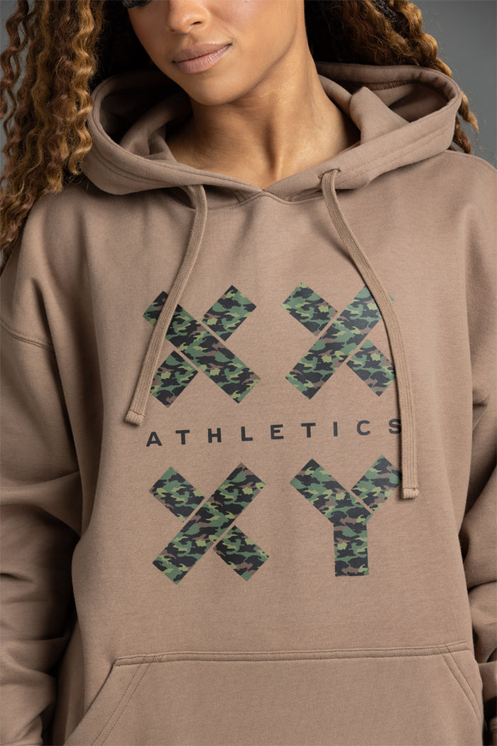 Person wearing a beige hoodie with camouflage 'ATHLETICS' text design. || Mocha