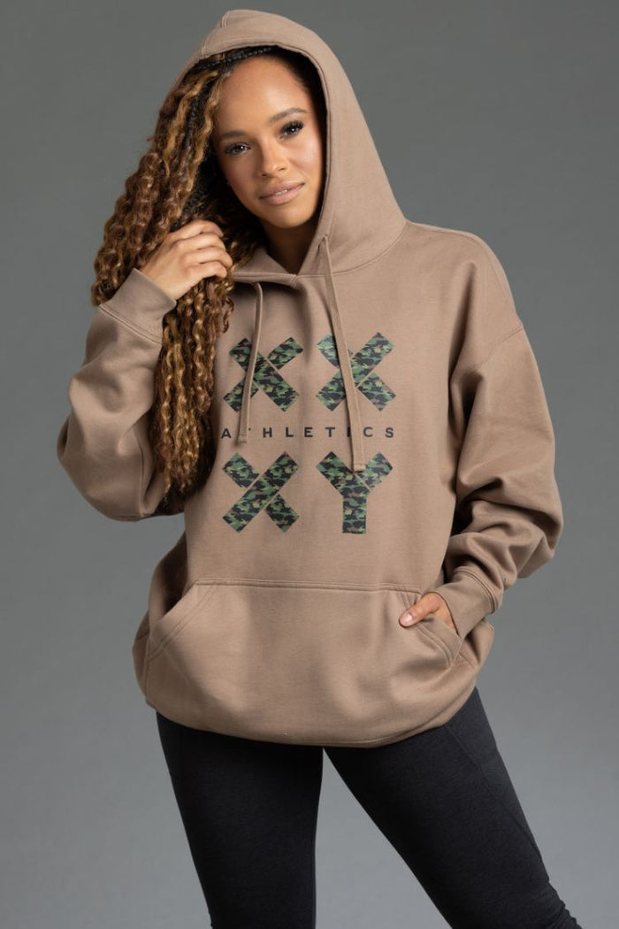 Person wearing a beige hoodie with a brand logo on a gray background || Mocha